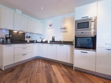 A kitchen with white cabinets a microwave oven a coffee maker a toaster and wooden floor at Abalone in St Ives