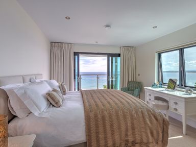A bedroom with a bed a desk and a chair overlooking the sea at Abalone in St Ives