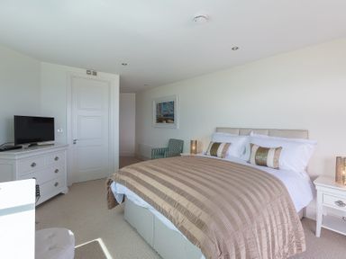 A bedroom with a bed striped bedding a TV on a dresser and a chair at Abalone in St Ives