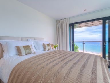 A bedroom with a striped bedspread and pillows near a glass door with a view of the ocean at Abalone in St Ives