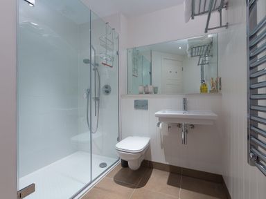 A bathroom with a glass shower enclosure wall-mounted toilet and sink at Abalone in St Ives