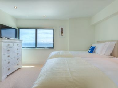 A bedroom with two beds a white chest of drawers and a window with a sea view at Abalone in St Ives