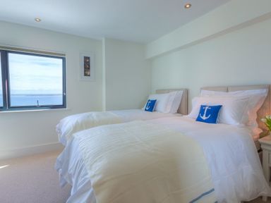 A bedroom with two beds and a window showing the sea at Abalone in St Ives