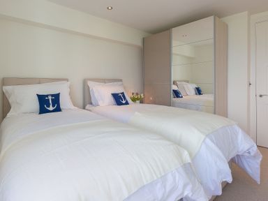 A bedroom with two single beds with white bedding and blue anchor pillows and a mirrored wardrobe at Abalone in St Ives