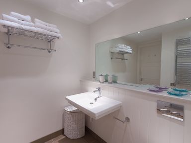 A bathroom with a white sink a wicker laundry basket and folded towels on a wall rack at Abalone in St Ives