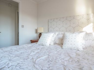 A bedroom with a bed with floral bedding and pillows a bedside table with a lamp and an open door at Oak Lodge in Glasshouse
