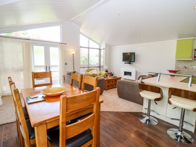 A dining table with six chairs next to a living area with sofas and a wall mounted tv at Oak Lodge in Glasshouse