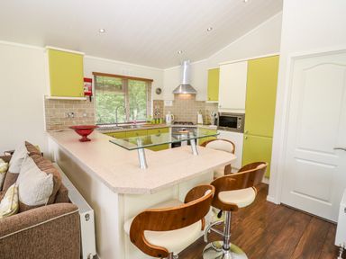 A kitchen with green cabinets a glass counter and wooden bar stools at Oak Lodge in Glasshouse