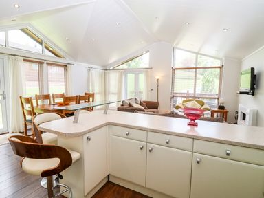 An open kitchen and living area with a dining table wooden chairs sofas and a wall mounted television at Oak Lodge in Glasshouse