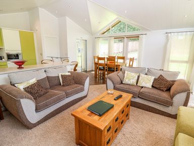 A living room with two brown and beige sofas around a wooden coffee table next to a dining table and kitchen at Oak Lodge in Glasshouse