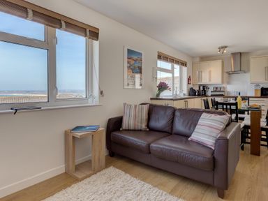A living room with a brown leather sofa and striped cushions next to a wooden side table and window with a view at Atlantic Blue in Carbis Bay
