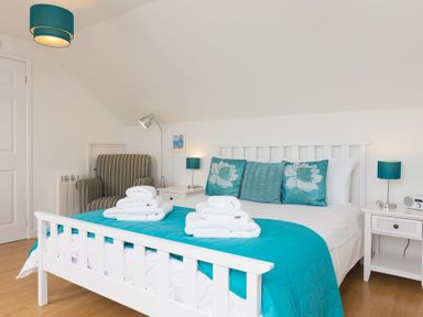 A bedroom with a white bed blue pillows and blanket a striped armchair and two bedside tables at Atlantic Blue in Carbis Bay