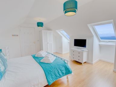 A bedroom with a bed towels a wardrobe a chest of drawers and two windows with sea views at Atlantic Blue in Carbis Bay