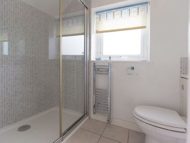 A bathroom with a shower enclosure a toilet a towel rack and a window at Atlantic Blue in Carbis Bay