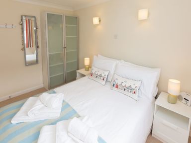 A bedroom with a double bed two bedside tables with lamps a wardrobe and a wall mirror at Atlantic Blue in Carbis Bay