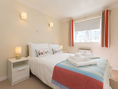 A bedroom with a double bed bedside tables lamps and a window with striped curtains at Atlantic Blue in Carbis Bay