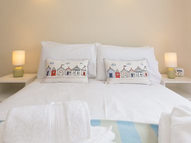 A bedroom with a bed with white linens and decorative pillows and two bedside tables with lamps at Atlantic Blue in Carbis Bay