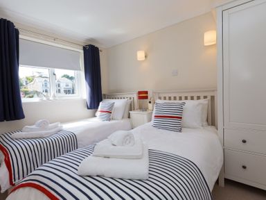A bedroom with two single beds with striped bedding and a window with dark curtains at Atlantic Blue in Carbis Bay