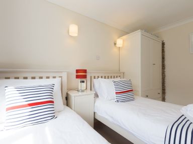 A bedroom with two single beds striped pillows a bedside table with a red lamp and a white wardrobe at Atlantic Blue in Carbis Bay