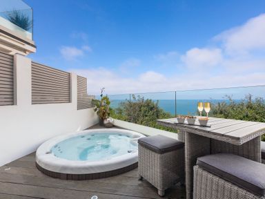A balcony with a hot tub a wicker table and stools and ocean view at Atlantic Watch 8 in Carbis Bay