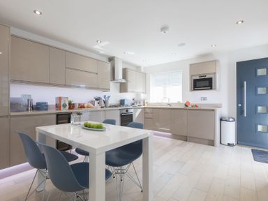 A modern kitchen with beige cabinets a white dining table with blue chairs and a blue door at Atlantic Watch 8 in Carbis Bay