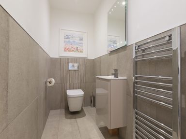 A bathroom with a wall-mounted toilet a sink unit a mirror a chrome towel rack and a framed picture at Atlantic Watch 8 in Carbis Bay