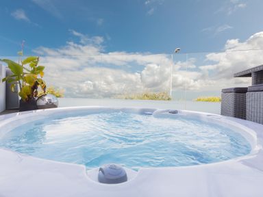 An outdoor hot tub with water and plants on the side under a cloudy sky at Atlantic Watch 8 in Carbis Bay