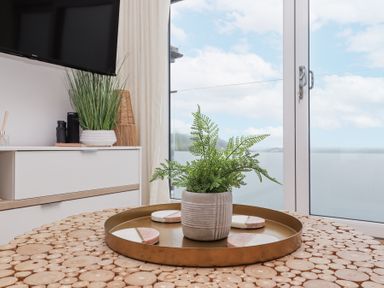 A wooden round table with a brass tray holding a potted plant and coasters in front of a glass door with a water view at Atlantic Watch 8 in Carbis Bay