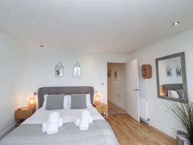 A bedroom with a bed two bedside tables and lamps a large mirror and framed pictures on the wall at Atlantic Watch 8 in Carbis Bay