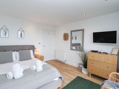 A bedroom with a bed, nightstand, dresser, wall mirror, TV, and decorative plants at Atlantic Watch 8 in Carbis Bay
