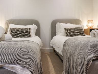 A bedroom with two single beds with grey headboards patterned blankets and bedside table with lamp at Atlantic Watch 8 in Carbis Bay