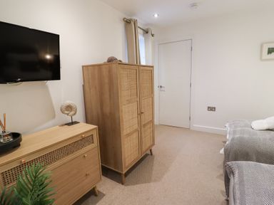 A bedroom with a wooden dresser and wardrobe a TV on the wall and a bed with gray blankets at Atlantic Watch 8 in Carbis Bay