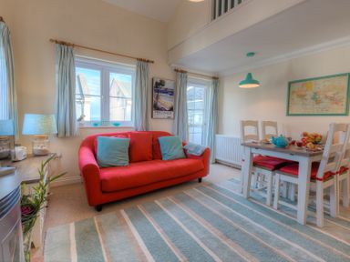 A living room with a red sofa and blue cushions next to a dining table with chairs and a map on the wall at Brinyloft in Carbis Bay