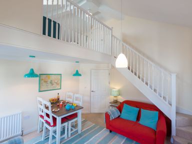 A dining area with a table and chairs next to a red sofa under a staircase at Brinyloft in Carbis Bay
