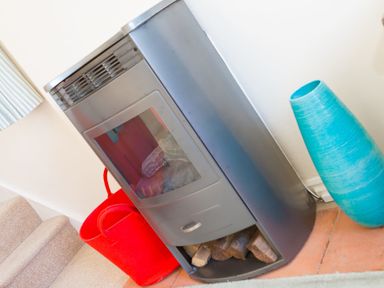 A metal wood stove with logs underneath a red basket and a blue vase standing on a tiled floor at Brinyloft in Carbis Bay