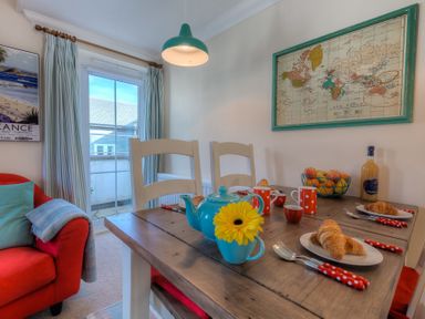 A dining area with a wooden table set for four with croissants cups and a teapot near a red armchair at Brinyloft in Carbis Bay