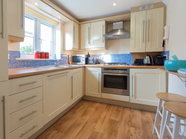 A kitchen with white cabinets wooden countertops blue tile backsplash and wooden floor at Brinyloft in Carbis Bay