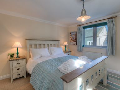 A bedroom with a large bed with folded towels on it two bedside tables with lamps and a window with curtains at Brinyloft in Carbis Bay