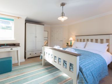 A bedroom with a bed covered with blue bedding a wardrobe a desk and a striped rug at Brinyloft in Carbis Bay