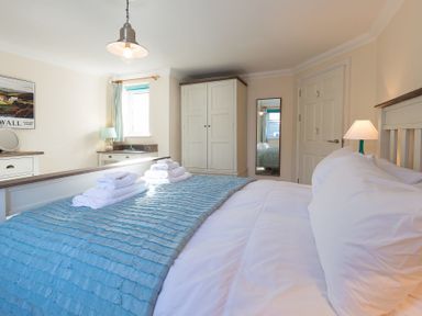 A bedroom with a bed covered by a blue blanket and folded towels on top a wardrobe a mirror a door a bedside lamp a dresser with a mirror and a window at Brinyloft Carbis Bay