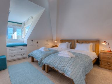 A bedroom with two single beds blue bedspreads wooden furniture and a window seat at Brinyloft in Carbis Bay
