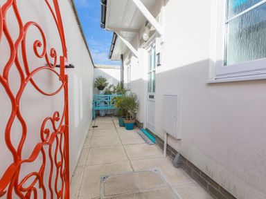 A narrow outdoor patio with a red metal gate blue bench potted plants and a white door at Brinyloft in Carbis Bay