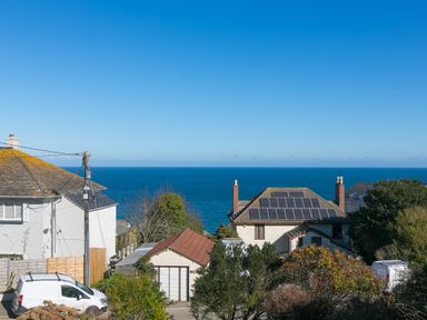 Houses with rooftops including one with solar panels and a van parked near them overlooking the ocean at Cornerways in Carbis Bay