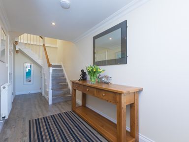 A hallway with a wooden console table holding a vase of flowers and decorative items and a mirror above it at Cornerways in Carbis Bay