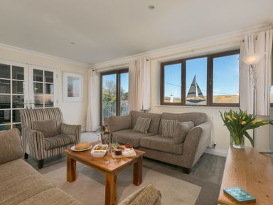 A living room with sofas a coffee table with snacks and drinks and a window with a sailboat decoration at Cornerways in Carbis Bay