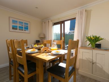 A dining room with a wooden table set for breakfast and a cabinet with flowers at Cornerways in Carbis Bay