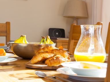 A dining table with croissants bananas and a glass jug of orange juice at Cornerways in Carbis Bay