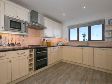 A kitchen with cream cabinets black countertops and wooden floor with a window at Cornerways in Carbis Bay