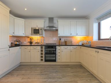 A kitchen with cream cabinets black countertops a stove microwave utensils bread bin and window at Cornerways in Carbis Bay