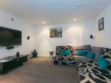 A living room with a mounted television and patterned sectional sofa with blue pillows at Cornerways in Carbis Bay